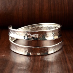May include: A silver hammered cuff bracelet with a double band design. The bracelet is made of metal and has a smooth, polished finish.