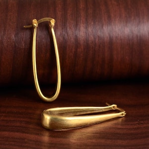 Puede incluir: Un par de pendientes de aro de oro. Los pendientes son de forma ovalada y tienen un acabado liso y pulido.