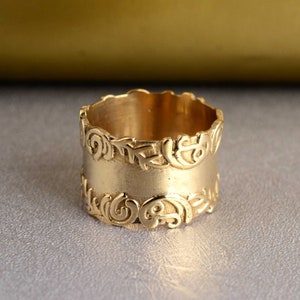 Puede incluir: Un anillo de oro con una banda ancha y diseños intrincados y en espiral alrededor de los bordes.