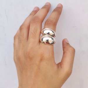 May include: Two silver rings stacked on a finger. The rings are smooth and rounded, with a shiny finish.