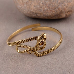 May include: A gold snake bracelet with a brown tiger's eye stone. The snake is coiled and the stone is set in the snake's head.