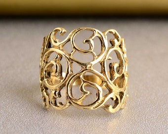 Puede incluir: Un anillo de filigrana dorado con un diseño delicado e intrincado. El anillo está hecho de una sola pieza de metal y tiene una banda ancha.