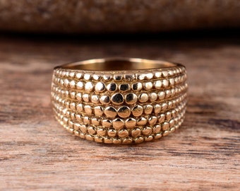 May include: A gold-toned ring with a textured, patterned design. The ring is made of multiple rows of small, round, raised dots.