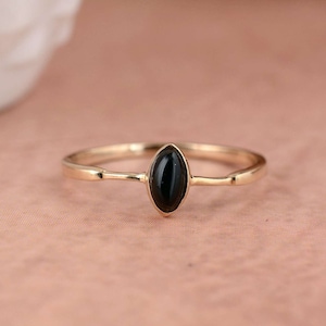 Puede incluir: Un delicado anillo de oro con una piedra ovalada negra. El anillo tiene un diseño simple y minimalista.
