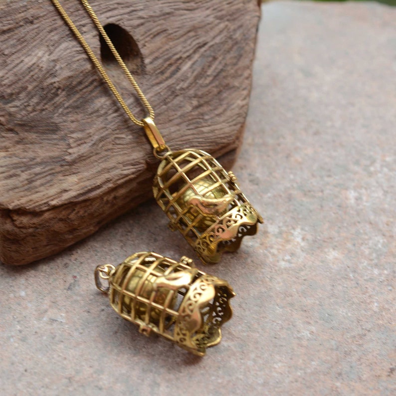 Puede incluir: Un collar de oro con un colgante que representa un p&aacute;jaro dentro de una jaula. La jaula est&aacute; intrincadamente detallada y tiene un dise&ntilde;o delicado. El colgante est&aacute; unido a una cadena de oro.