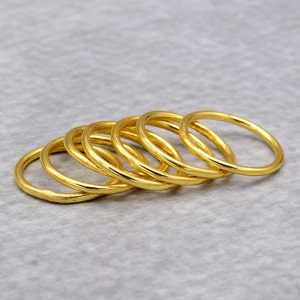 May include: A set of six gold-coloured stacking rings. The rings are smooth and have a slightly rounded shape.