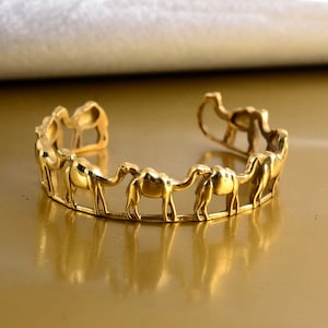 May include: A gold-toned metal bracelet featuring a continuous design of camels walking in a circle.
