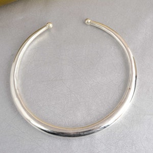 Könnte beinhalten: Eine silberne Choker-Kette mit einer glatten, abgerundeten Oberfläche.
