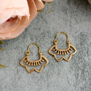 May include: A pair of gold-toned hoop earrings with a delicate, intricate design. The earrings feature a scalloped edge and a central motif of small, rounded shapes.