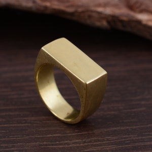 Peut inclure: Une bague rectangulaire de couleur dorée avec une surface lisse et plate.