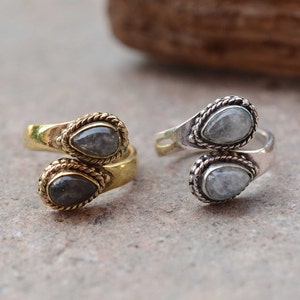 May include: Two adjustable rings with a silver and gold finish. Each ring features two teardrop-shaped stones with a cloudy white color.