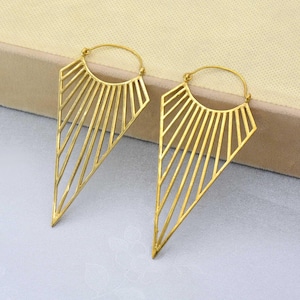 Puede incluir: Un par de pendientes de aro geométricos de color dorado con forma triangular y diseño de rayos de sol.
