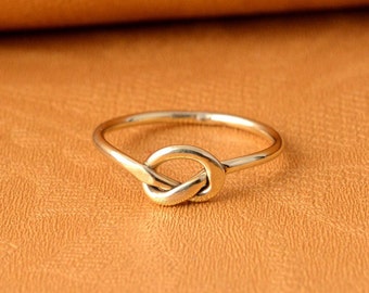 May include: A gold knot ring with a simple design. The ring is made of a smooth metal and has a polished finish.