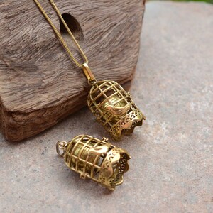 Puede incluir: Dos colgantes de jaula de p&aacute;jaros de tono dorado con un peque&ntilde;o p&aacute;jaro dentro. El colgante m&aacute;s grande est&aacute; en una cadena dorada.