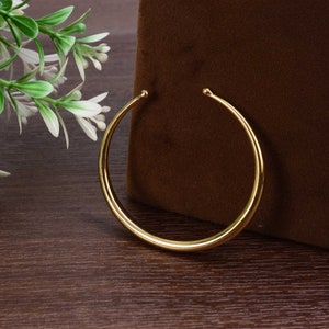 May include: A simple gold bangle bracelet with a smooth, rounded finish.