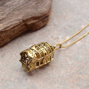 Puede incluir: Un collar dorado con un colgante en forma de jaula que contiene una peque&ntilde;a bola. El colgante est&aacute; intrincadamente detallado y tiene un dise&ntilde;o delicado.