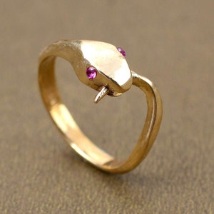 May include: A gold snake ring with two pink gemstones for eyes.