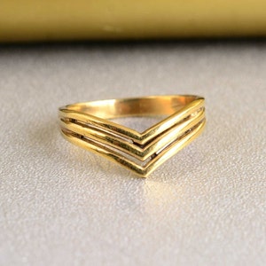 Op de afbeelding: Een ring van goudkleurig metaal met een drievoudig chevron-ontwerp. De ring heeft een eenvoudige, moderne stijl.