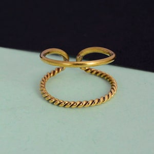 Può includere: Un anello dorato con un design a fascia intrecciata. L'anello è aperto da un lato e ha una finitura liscia e lucida.