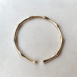 Op de afbeelding: Een gouden armband met een bamboe-ontwerp. De armband is open en heeft een gladde, gepolijste afwerking.