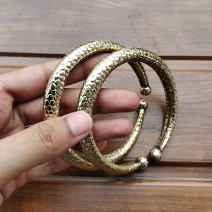 May include: Two gold-colored metal bangles with a textured surface. The bangles are stacked on top of each other.