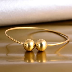 May include: A gold bangle bracelet with two large, round, gold beads.