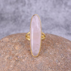 May include: A gold ring with a large oval-shaped pink rose quartz gemstone.