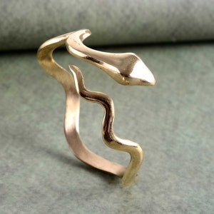 May include: A gold-toned snake-shaped bracelet with a wavy design. The bracelet is open and can be adjusted to fit different wrist sizes.