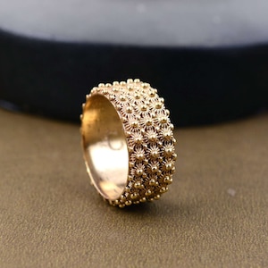 Op de afbeelding: Een gouden bandring met een getextureerd oppervlak van kleine verhoogde cirkels die een bloemvormig patroon vormen.