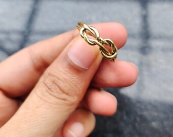 May include: A gold-toned ring with a knot design. The ring is worn on a finger.