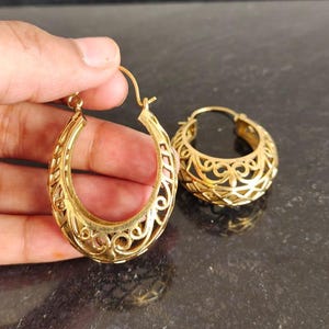 May include: A pair of gold hoop earrings with a delicate, intricate design. The earrings are made of a lightweight metal and have a slightly curved shape.