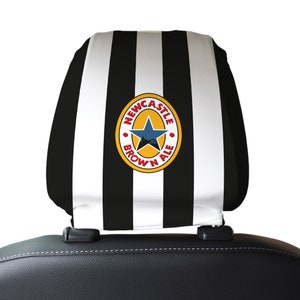 Puede incluir: Reposacabezas de asiento de coche a rayas blancas y negras con un logotipo circular marr&oacute;n y amarillo que dice "Newcastle Brown Ale" con una estrella y un puente dentro del c&iacute;rculo.