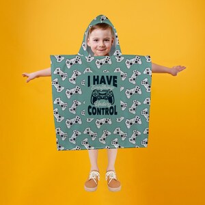 May include: A teal hooded poncho featuring a pattern of white game controllers. The text "I Have Everything Under Control" is printed in black and white. The background is a solid yellow.