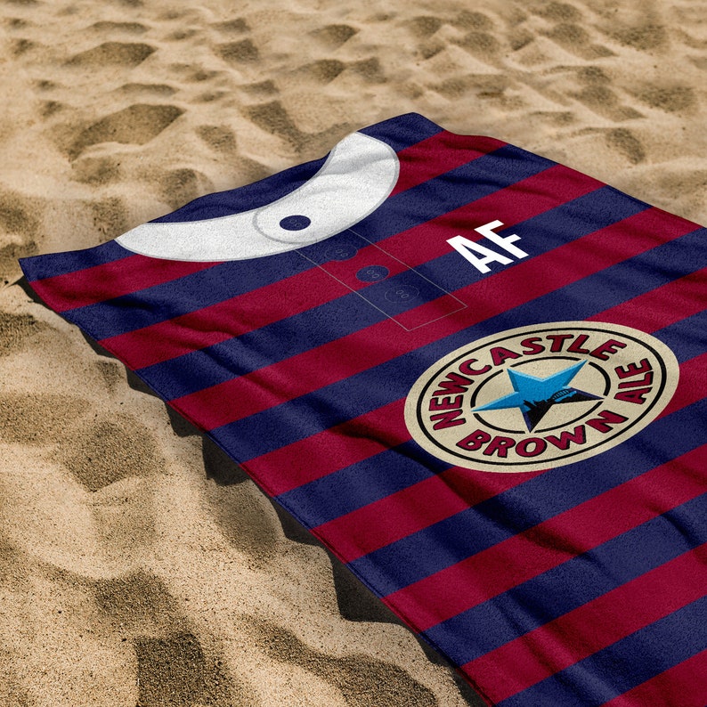 Peut inclure: Une serviette de plage ray&eacute;e rouge et bleue avec un col blanc et le texte "AF" sur le devant. La serviette pr&eacute;sente &eacute;galement un logo circulaire avec le texte "Newcastle Brown Ale".
