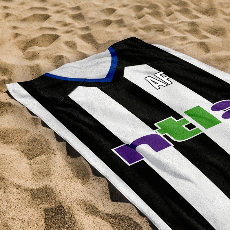 May include: Black and white striped beach towel with a blue and white stripe across the top. The towel has the letters "AF" and the word "ntla" in green and purple letters.