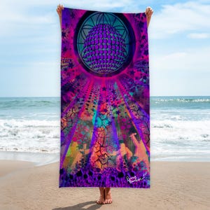 Könnte beinhalten: Ein lebendiges Strandtuch mit psychedelischem Design. Es zeigt eine große, lila, kugelförmige Form oben, die farbige Strahlen aussendet. Das Handtuch hat eine Signatur unten rechts und wird am Strand gehalten.