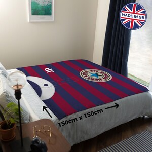 May include: A red and blue striped fleece blanket with a Newcastle Brown Ale logo and the initials "JP". The blanket is 59 inches by 59 inches.