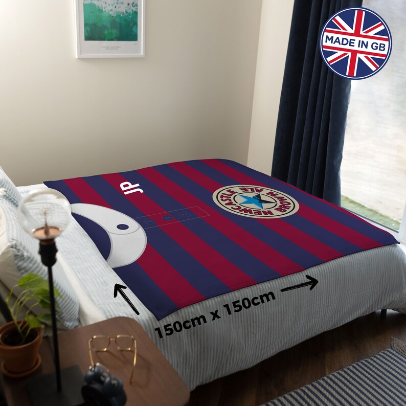 May include: A red and blue striped fleece blanket with a Newcastle Brown Ale logo and the initials "JP". The blanket is 59 inches by 59 inches.
