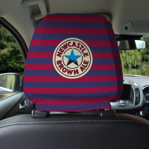 Op de afbeelding: Een blauwe en rode gestreepte hoofdsteun voor autostoelen met een wit cirkelvormig logo met de tekst "Newcastle Brown Ale" met een blauwe ster en een skyline van de stad in de cirkel.