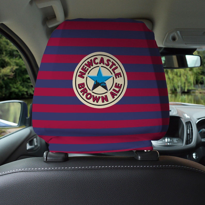 Op de afbeelding: Een blauwe en rode gestreepte hoofdsteun voor autostoelen met een wit cirkelvormig logo met de tekst "Newcastle Brown Ale" met een blauwe ster en een skyline van de stad in de cirkel.