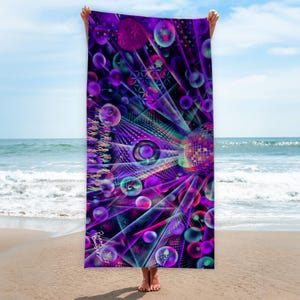 Könnte beinhalten: Ein lebendiges Strandtuch mit einem psychedelischen Design mit einer Discokugel, geometrischen Formen und Blasen in Lila-, Türkis- und Rosatönen. Das Tuch wird vor einem Strand- und Ozeanhintergrund gehalten.