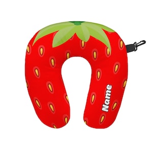 Op de afbeelding: Rode en groene nek kussen voor reizen in de vorm van een aardbei met het woord "Naam" erop gedrukt.