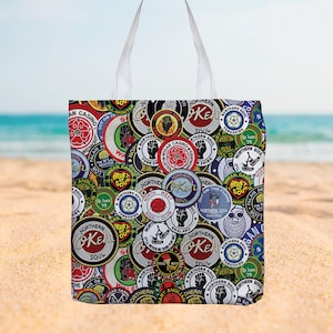 May include: A white tote bag with a vibrant collage of circular patches. The patches display text and graphics, including "Northern Soul" and "Wigan Casino." The bag has white handles and is set against a beach backdrop, evoking a seaside theme.