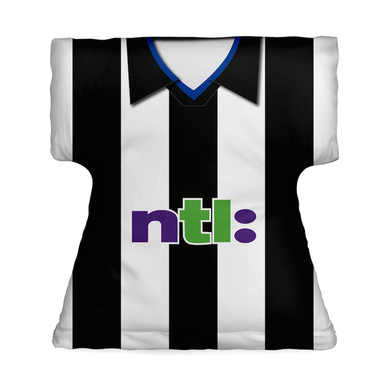 May include: A cushion shaped like a black and white striped football shirt. The shirt features a collar with blue trim and the word "ntl:" in purple and green. The sides of the cushion are white.