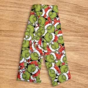 Könnte beinhalten: Grüne und rote Weihnachts-Leggings mit einem sich wiederholenden Muster eines grünen Gesichts mit Weihnachtsmütze. Die Leggings sind auf einer Holzoberfläche gefaltet.