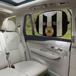 May include: Black and white striped car window sunshade with the text "ADD ANY TEXT" and a Newcastle Brown Ale logo. The sunshade is oval-shaped and attached to the car window.