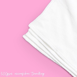 May include: A stack of four white microfiber towels on a pink background. 300gsm microfiber toweling.