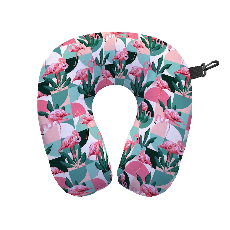 May include: A pink and green travel neck pillow with a flamingo pattern. The pillow is shaped like a horseshoe and has a strap to secure it around the neck.