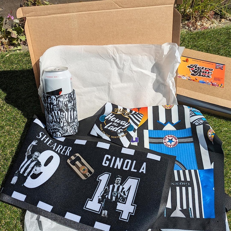 May include: An open cardboard box containing a Newcastle United football-themed gift set. Includes a black and white can cooler, a black and white towel with player names and numbers, and a jersey-style scarf. A Retro Star Box sticker is visible.