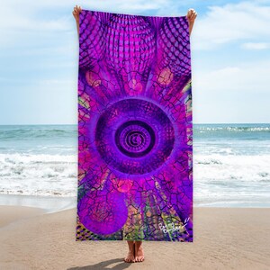 Könnte beinhalten: Ein lebendiges Strandtuch mit einem psychedelischen Design in Lila-, Rosa- und Grüntönen. Das Tuch zeigt ein zentrales kreisförmiges Muster mit konzentrischen Ringen und einem rissigen, strukturierten Hintergrund. Das Tuch wird an einem Sandstrand hochgehalten.